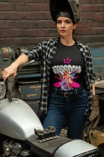 Person wearing a graphic t-shirt with a crown design and plaid shirt, standing next to a motorcycle.