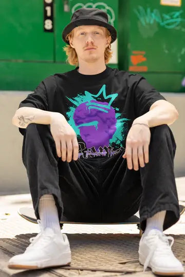 Person sitting on a skateboard wearing a black t-shirt with a colorful graphic design, black hat, and white sneakers.