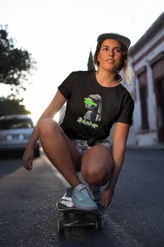 Person wearing a black t-shirt with a graphic design, sitting on a skateboard outdoors.