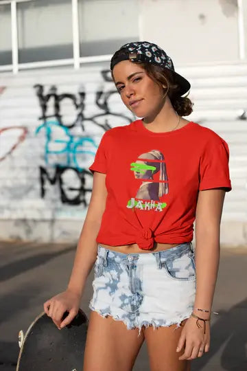Woman wearing a red t-shirt with a graphic design and denim shorts, standing in front of a graffiti-covered wall.